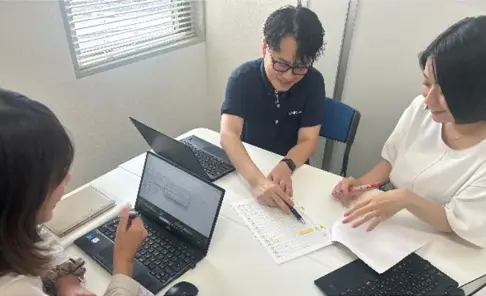 ノートパソコンと資料を囲み情報共有を行うディ・エム・シーの担当者ミーティング